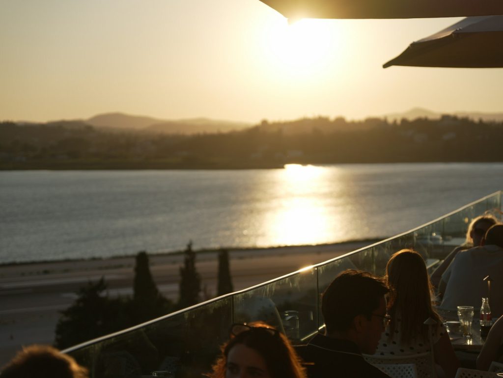 Grupo de personas disfrutando una copa de vino viendo el atardecer desde una terraza junto al mar